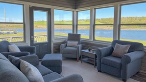 Een gezellige kamer met een groot raam met uitzicht op een meer, een comfortabele zithoek en een kleine tafel.