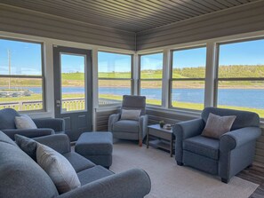 Una habitación acogedora con un amplio ventanal con vistas a un lago, una zona de estar confortable y una mesita.