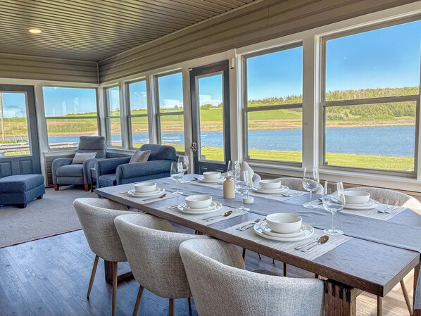 Uma sala de jantar com uma mesa posta para seis pessoas, grandes janelas e vista para um lago.