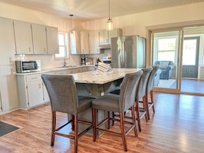 A modern kitchen with a central island, bar stools, stainless steel appliances, and a view to the outside.