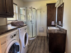 Casa de banho compacta com máquina de lavar roupa, cabine de duche em vidro e lavatório com espelho.