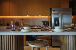 A modern kitchen with a central island, wooden stools, and a stainless steel refrigerator. - 1BR Penthouse in Aflora condo w/ Private Pool (Tulum)