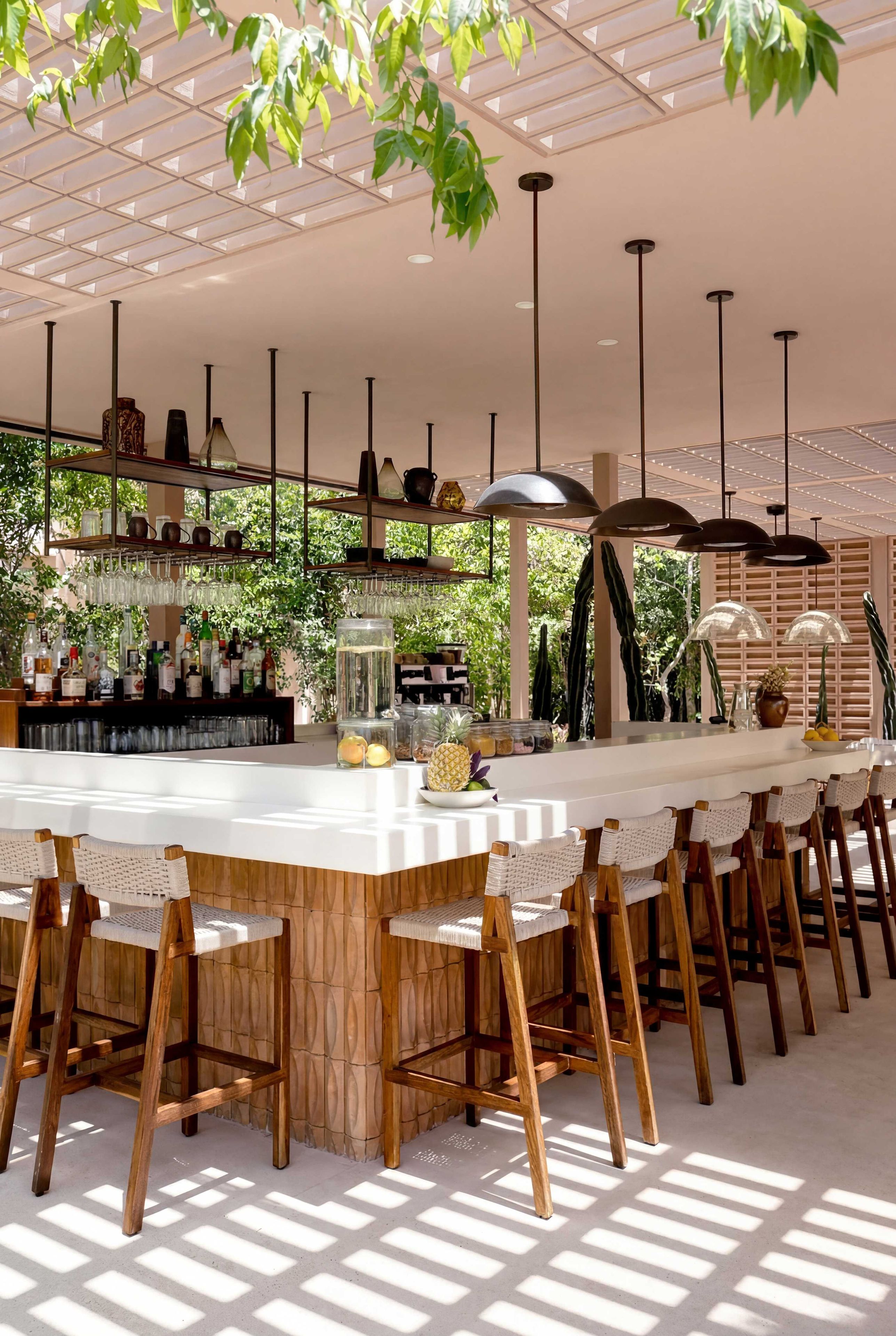 A modern bar area with a central island, bar stools, hanging pendant lights, and a ceiling with a geometric pattern.