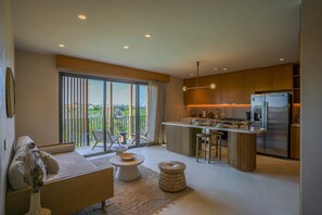 A modern kitchen with a large island, a dining area with a sofa and table, and a balcony with a view. - 1BR Penthouse in Aflora condo w/ Private Pool (Tulum)
