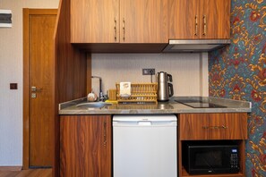 A compact kitchen with wooden cabinets, a dishwasher, a microwave, a kettle, and a sink. - Hanchi BY Ottoman Suites (İstanbul)