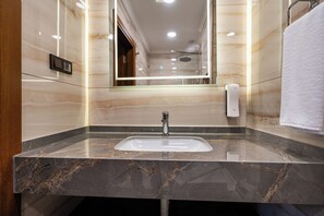 Un baño con lavamanos de mármol, un espejo, toallero y cabezal de ducha de mano.