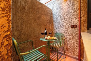 Rincón con pared texturizada, una pequeña mesa con una botella y copas, y dos sillas.