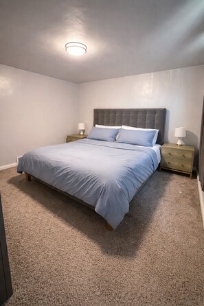 Un dormitorio con una cama grande, dos mesitas de noche con lámparas, una luz en el techo y suelo alfombrado.