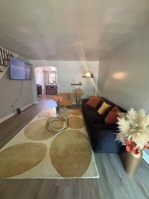 Una sala de estar con sofá, mesa de centro y televisor en la pared.