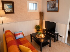 Ein Wohnzimmer mit einer Couch, einem Fernseher, einem kleinen Tisch mit einer Pflanze und einem Fenster.