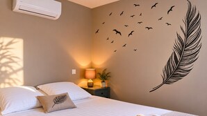 Ein Schlafzimmer mit Bett, Kissen, einem Nachttisch mit Lampe, einer Wanddekoration mit Vögeln und einer Feder sowie einer Klimaanlage.