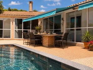 Ein Poolbereich mit Tisch und Stühlen, ein Ziegelpflanzgefäß mit einer Pflanze und ein klares Schwimmbecken.
