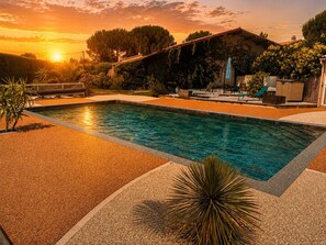 A rectangular swimming pool with a tiled deck, surrounded by a landscaped garden with various plants and a wooden fence. - Air-conditioned gîte with swimming pool 12x6 m, terrace and barbecue near beaches (Marsillargues)