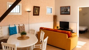 Ein Wohnzimmer mit einem runden Tisch, weißen Stühlen, einem gelben Sofa und einem Fernseher.