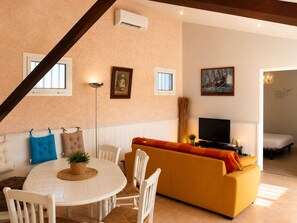 Ein Wohnzimmer mit einem runden Tisch, weißen Stühlen, einem gelben Sofa und einem Fernseher.