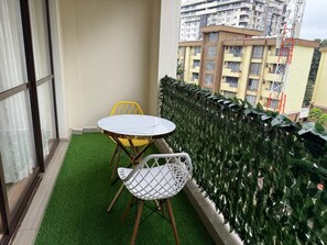 A balcony with a round table and two chairs, a green artificial grass floor, and a view of a building with multiple balconies. - Cozy 1 bedroom apartment in Kileleshwa (PQCM+HQH, Nairobi)