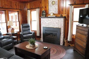 Ein Zimmer mit Kamin, Ledersesseln, Fernseher und Holzwänden.