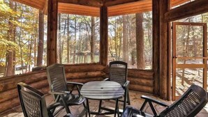 Uma cabana de madeira com uma mesa redonda e quatro cadeiras, cercada por grandes janelas que oferecem vista para uma área arborizada.