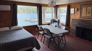 Quarto com cama, mesa com cadeiras, lareira e vista para um lago com barcos.