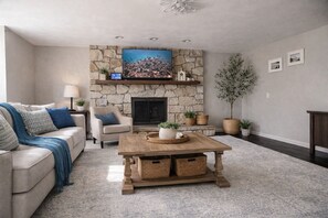 A living room with a stone fireplace, a television mounted above it, a wooden coffee table, a sofa, and a potted plant.