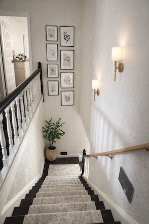 A staircase with a white railing, a potted plant, and framed botanical prints on the wall.