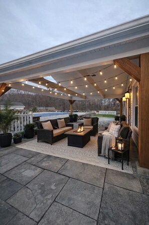 Un patio exterior con asientos, una chimenea, luces colgantes y vistas al paisaje.