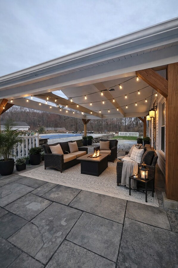 An outdoor patio with seating, a fire feature, string lights, and a view of the landscape.