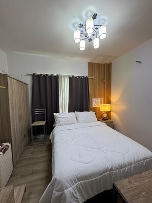 Een hotelkamer met een bed, een stoel, een kledingkast, een nachtkastje met lamp en een plafondlamp.