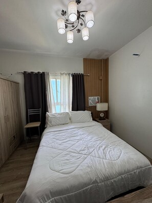 Een slaapkamer met een bed, een stoel, een kledingkast, een nachtkastje, een lamp en een plafondarmatuur.