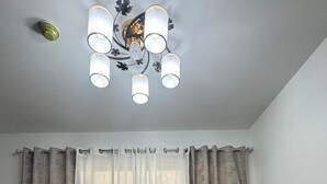 A bedroom with a bed, curtains, a ceiling light fixture, and a trash bin.