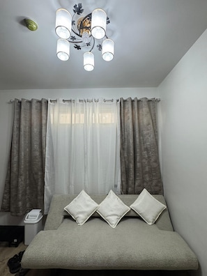 Un dormitorio con cama, cortinas, una lámpara de techo y un cubo de basura.