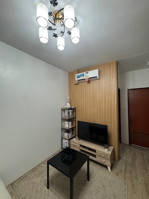 Una sala de estar con televisor, pared de paneles de madera, aire acondicionado e iluminación en el techo.