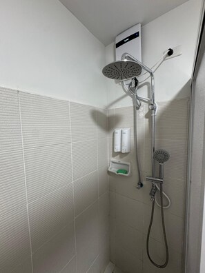 Una ducha con cabezal de ducha de mano, grifo empotrado y dispensador de jabón.