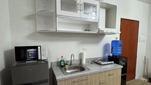 A compact kitchen with a refrigerator, a microwave, a sink, and a water dispenser.