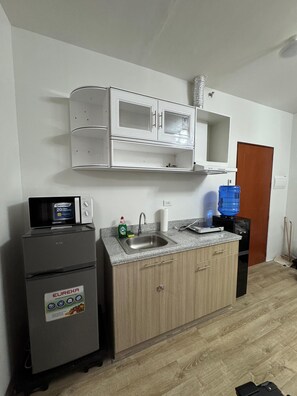 Una cocina compacta con refrigerador, microondas, lavaplatos y dispensador de agua.