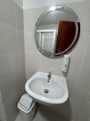 A bathroom with a white sink, a round mirror, and a hand sanitizer dispenser.