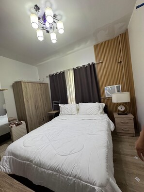 Een hotelkamer met een groot bed, een kledingkast, een nachtkastje met een lamp en een plafondarmatuur.