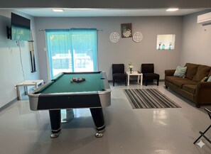Una mesa de billar en una sala con un sofá, sillas y decoración en la pared.