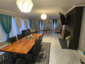 Un comedor con una mesa de madera, sillas, un tapete y un televisor montado en la pared.