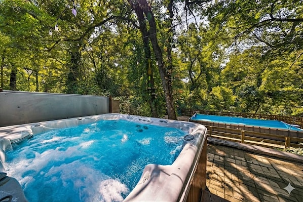 Un jacuzzi rodeado de árboles, con un muelle de madera y una piscina al fondo.