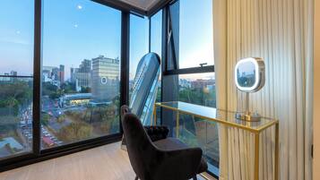A modern room with a large window, a chair, a desk with a mirror, and a city view.