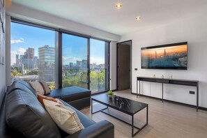 Ein modernes Wohnzimmer mit großem Fenster, einer schwarzen Ledersofa, einem Couchtisch und einem flachbildfernseher, der an der Wand angebracht ist.