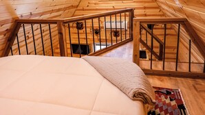 L'intérieur d'une cabane en bois, avec un lit, une fenêtre et un escalier.
