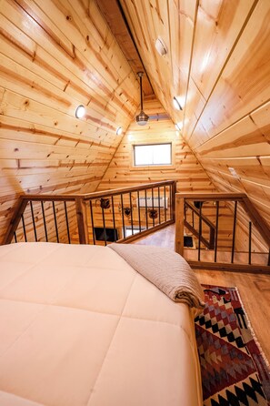 Ein Holzblockhaus-Interieur mit einem Bett, einem Fenster und einer Treppe.