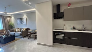 Una sala de estar moderna con un sofá, una mesa de centro y una mesa de comedor. Una cocina con estufa, fregadero y armarios está contigua.