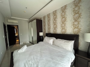A hotel room with a large bed, a mirror, a wardrobe, and a bathroom visible through an open door. - Lawrounds At Mirage  (Accra)