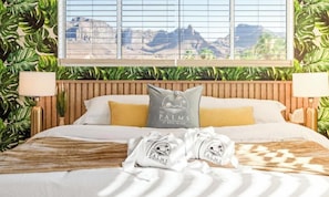 Ein Bett mit Blick auf Berge, ein hölzernes Kopfteil und zwei Kissen mit dem Aufdruck 'The Palms at Rock Island'.