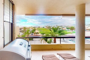 Een balkon met uitzicht op een golfbaan, een zwembad en ligstoelen.