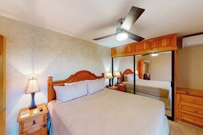 A bedroom with a bed, nightstands, a ceiling fan, a mirror, and wooden cabinets. - Inviting Apartment Across From the Beach With Pool, Grill, Balcony & Golf Nearby (San José del Cabo)