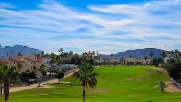 A golf course with palm trees, a flag, and buildings in the background.